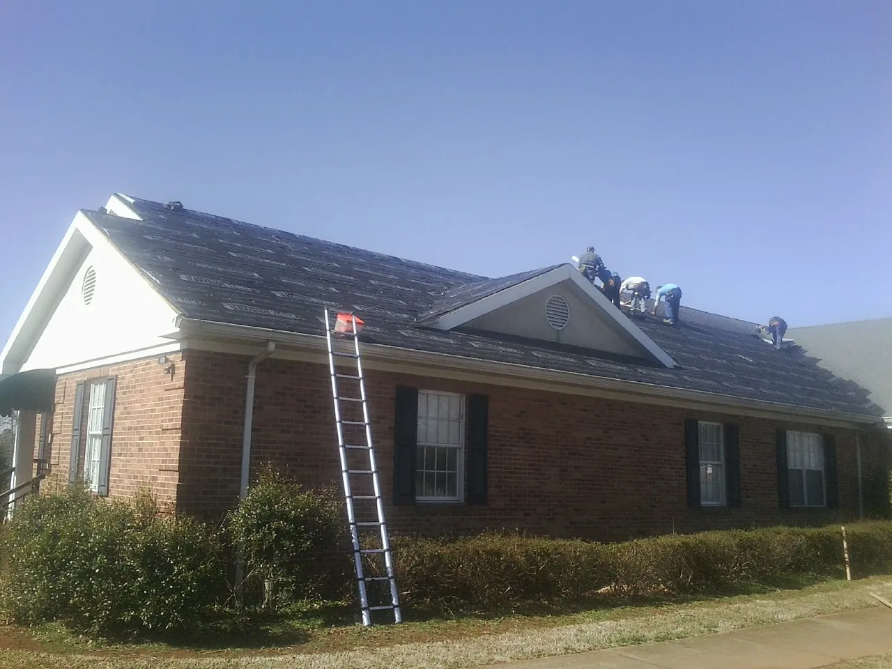 Crew tearing shingles off a brick ranch roof with a ladder set — Emergency Roof Repair work by our crew in Bechtelsville