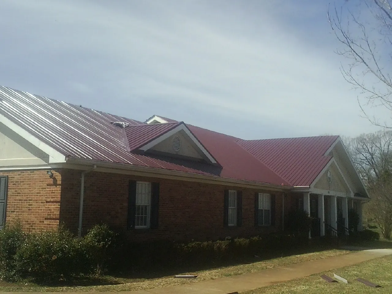 Red metal roof with gabled entries on a long brick building, from a Hail Damage Roof Repair job in Bechtelsville