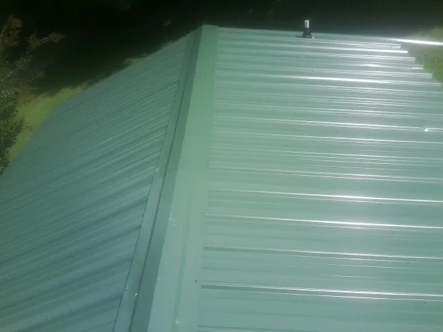 New green metal panels meeting at the ridge of a roof — Flat Roof Repair work by our crew in Bechtelsville