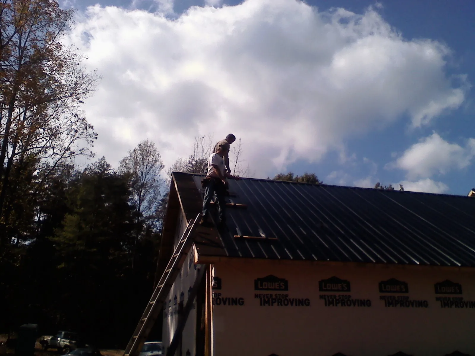 Roofer fastening dark metal panels high against a cloudy sky, from a Roof Inspection job in Bechtelsville