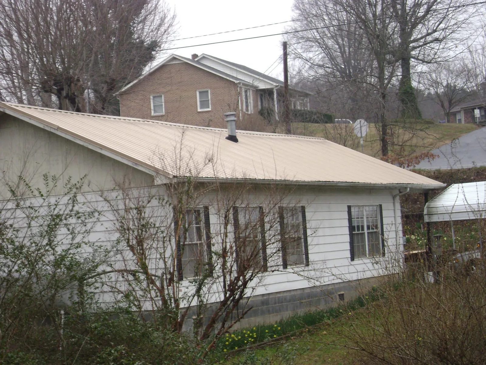 Tan metal roof on a white sided house set into a hillside — Commercial Roofing by Roofing Brothers in Bechtelsville